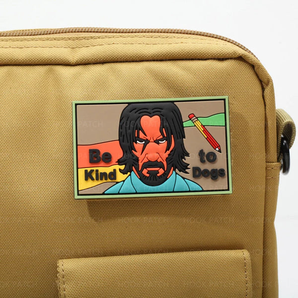 A rectangular patch featuring a stylized drawing of a dog with the text Be Kind to Dogs on a tan canvas bag.