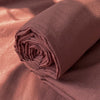 Rolled terracotta-colored organic cotton bedding set on a draped fabric.