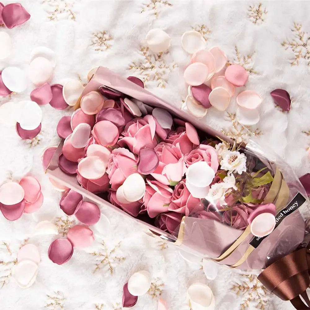 A glass jar filled with pink and white silk rose petals scattered on a white surface.