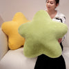 A person holds two star-shaped decorative throw pillows, one yellow and one light green.