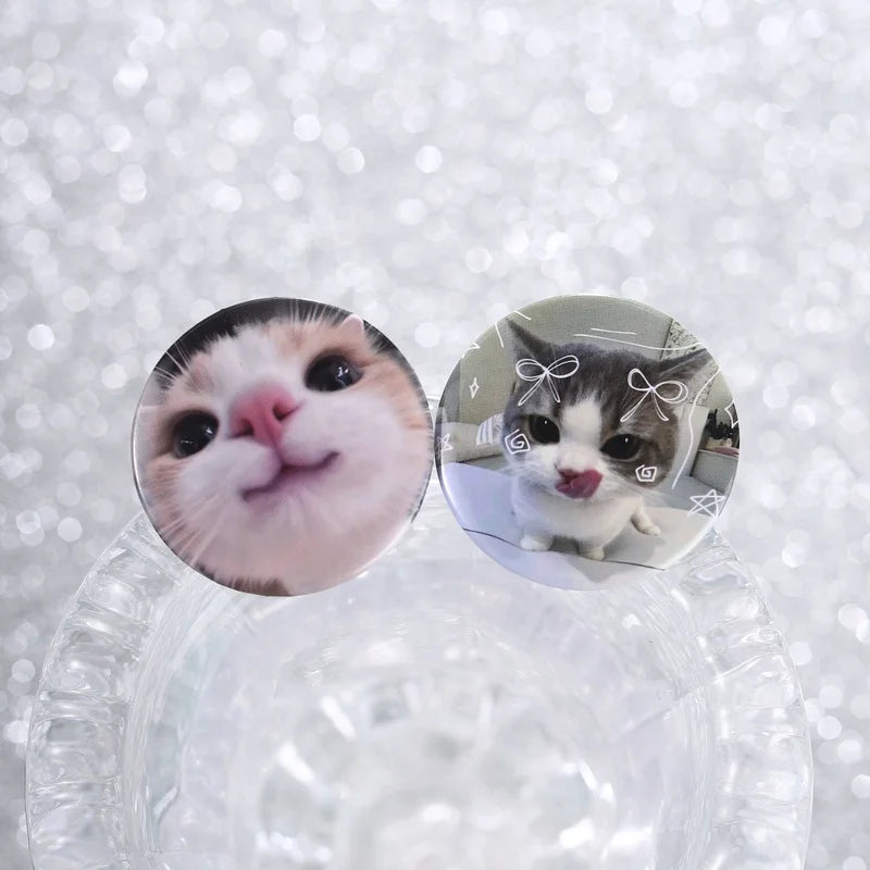 A pair of tinplate pin brooches featuring cute cat faces with expressive eyes and pink noses.