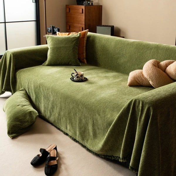 A moss green chenille sofa cover draped with pillows and a small cup on a light floor.