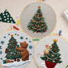 A hand embroidery kit featuring a detailed Christmas tree with a bear and snowflakes on a light background.