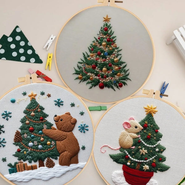 A hand embroidery kit featuring a detailed Christmas tree with a bear and snowflakes on a light background.