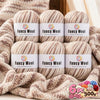 A set of three balls of fancy wool yarn in various shades of beige and brown stacked on a knitted fabric.