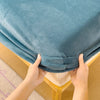 Hands folding a teal flannel fitted sheet with deep pockets on a wooden surface.