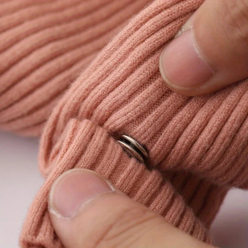 A hand is snapping a precision button onto a knitted garment in a dusty rose color.