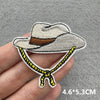 A hand holds a white cowboy hat iron-on patch with brown detailing and yellow stitching.