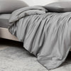 A smooth gray luxury bamboo duvet cover draped over a bed and resting on a light gray carpet.