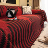 A deep red herringbone chenille sofa cover with black geometric patterns and tassel fringes on a sofa.