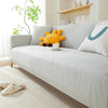 A light gray stretchable sofa cover with a vertical line pattern featuring yellow and white decorative pillows.