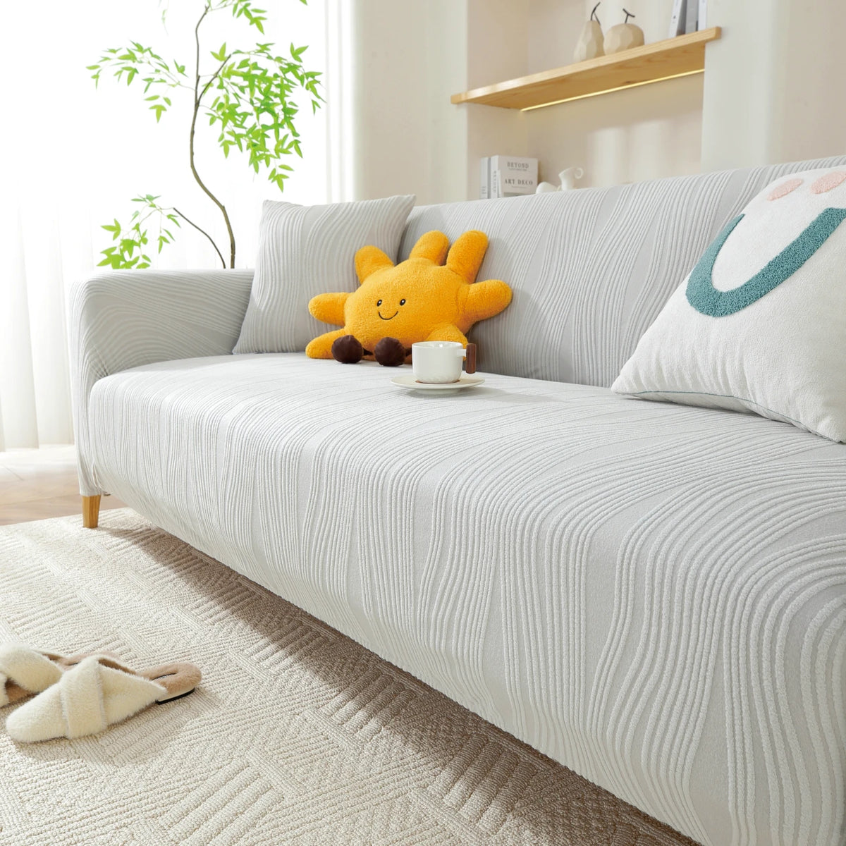 A light gray stretchable sofa cover with a vertical line pattern featuring yellow and white decorative pillows.