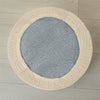A round, light beige ottoman footrest slipcover with a textured fabric and a gray circular insert.