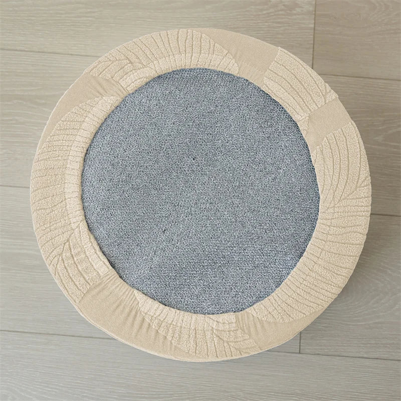 A round, light beige ottoman footrest slipcover with a textured fabric and a gray circular insert.