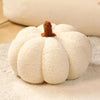 A white plush pumpkin throw pillow with a brown stem resting on a light surface.