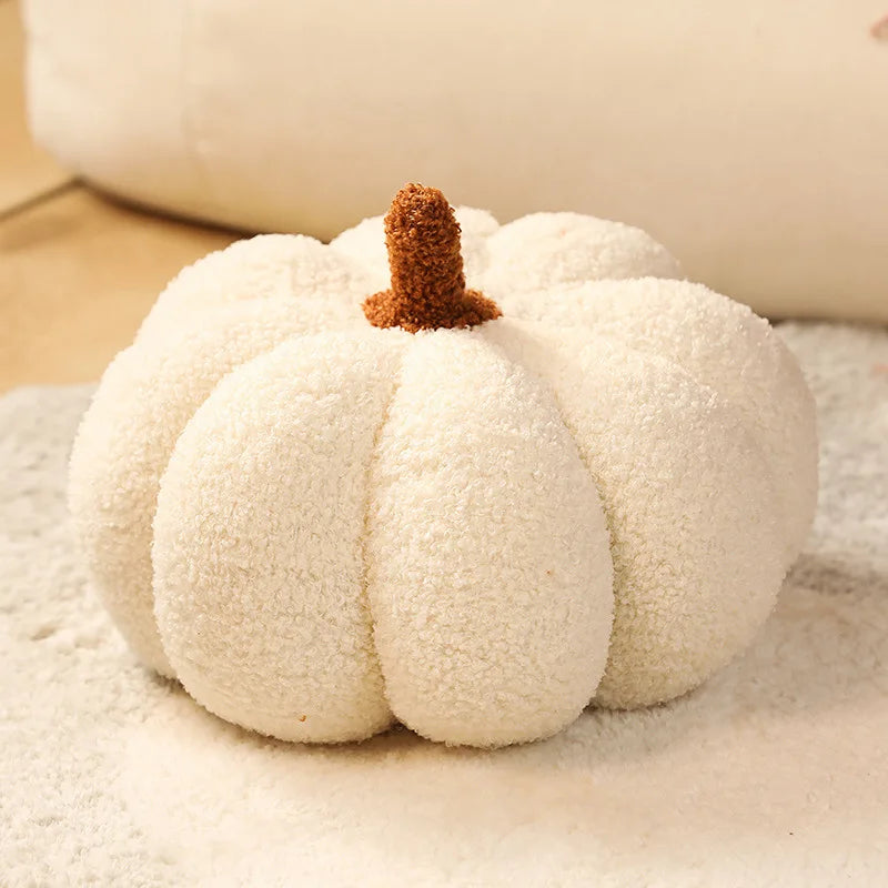 A white plush pumpkin throw pillow with a brown stem resting on a light surface.