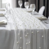 A white pearl beaded tulle table runner draped over a white tablecloth for an elegant event setting.