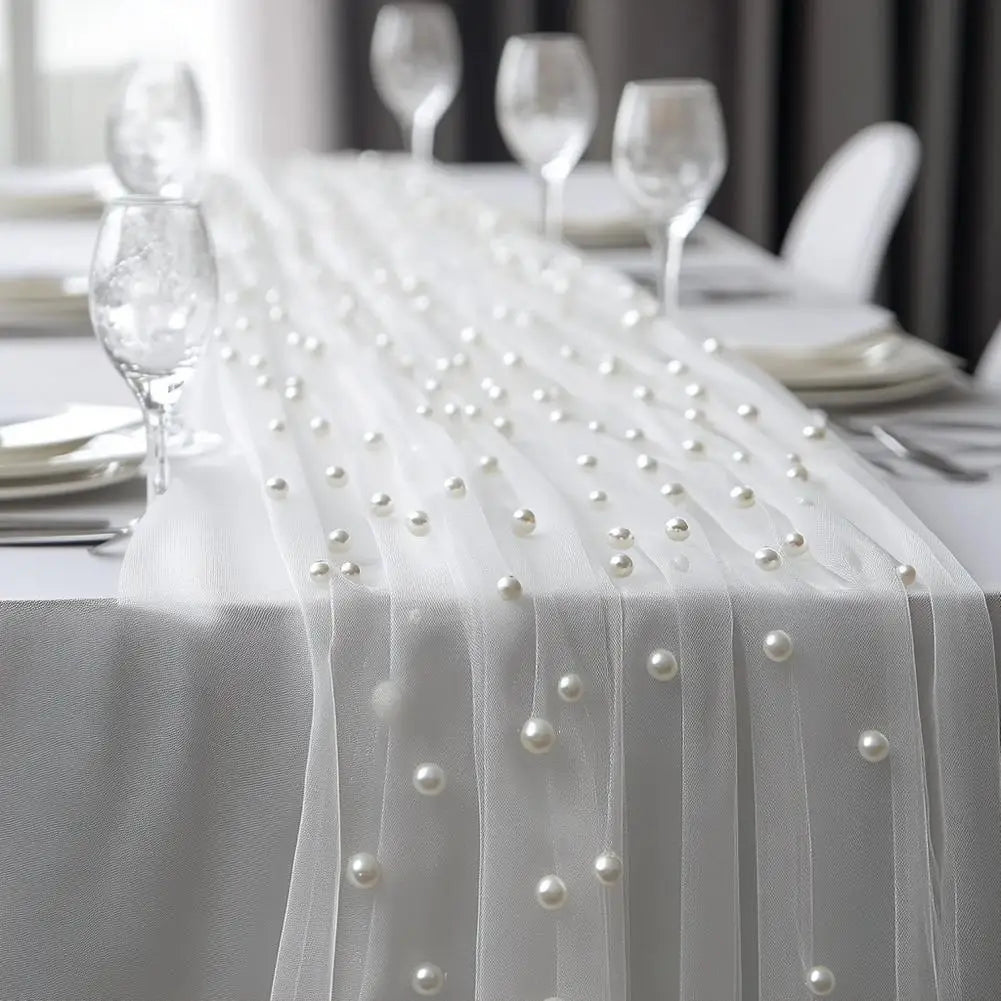 A white pearl beaded tulle table runner draped over a white tablecloth for an elegant event setting.