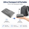 A gray inflatable travel neck pillow shown next to a black backpack and a hand, highlighting its compact size and portability