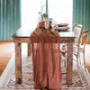 A rustic wooden table set with a sheer terracotta gauze table runner and elegant place settings.