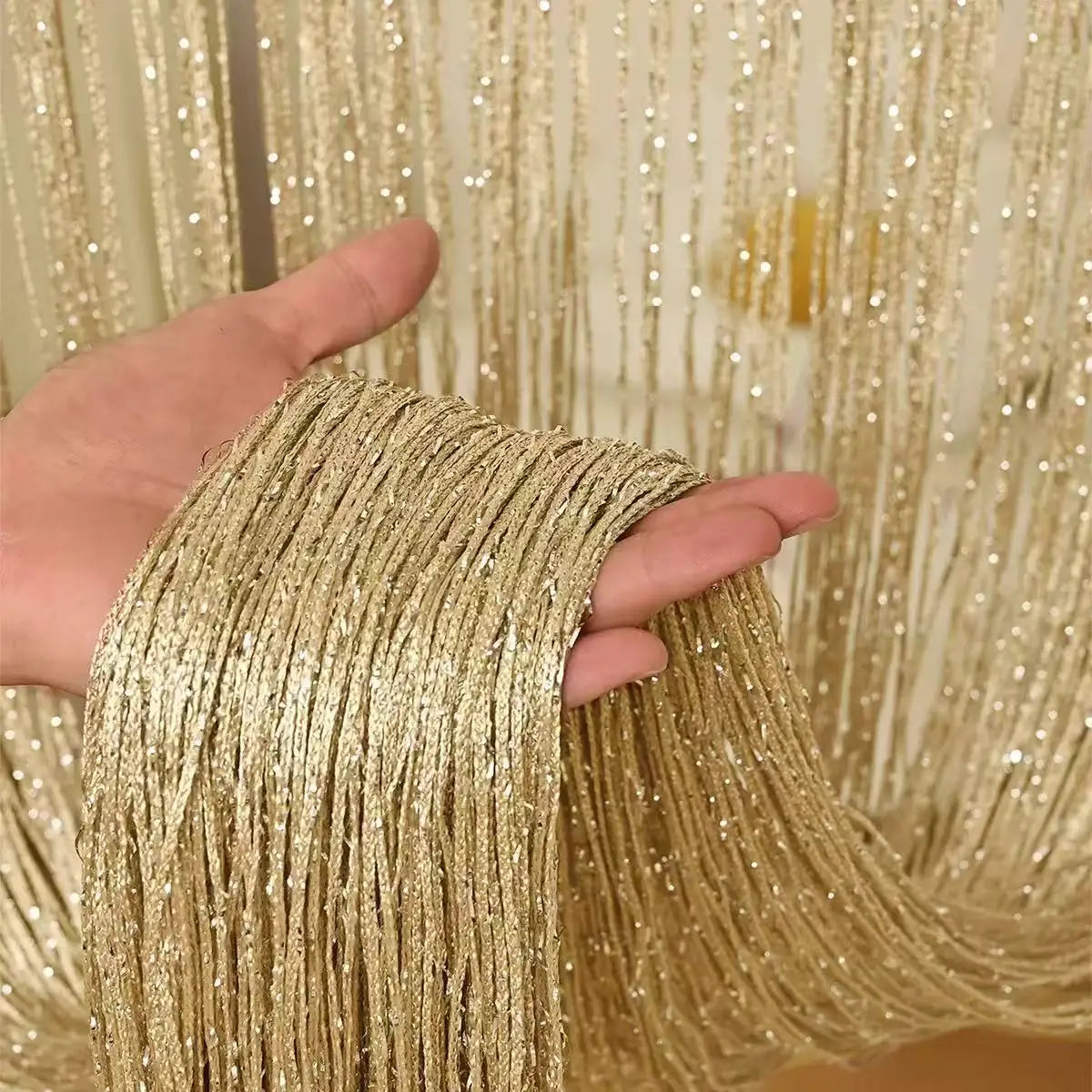 A hand is holding a bundle of gold metallic beaded string curtains for home and party decor.