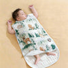 A baby is lying on a white sleeping bag patterned with woodland animals and greenery.