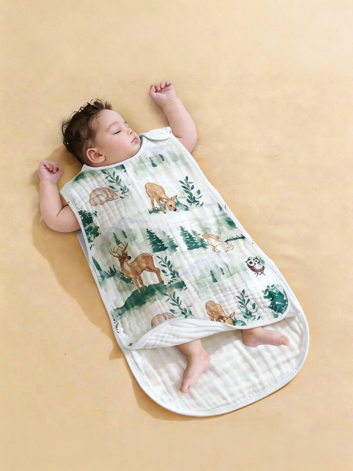 A baby is lying on a white sleeping bag patterned with woodland animals and greenery.