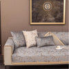 A luxurious sofa with light gray velvet cushion covers featuring gold foil accents, set against a neutral wall and framed art