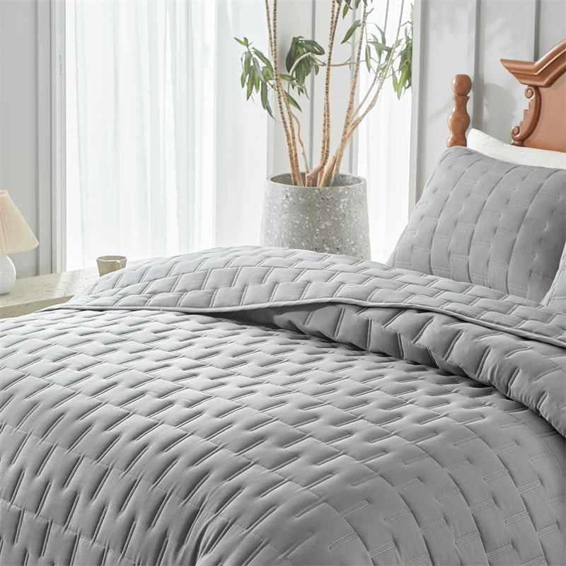 A gray quilted bedding set with a textured pattern is displayed on a bed next to a window.