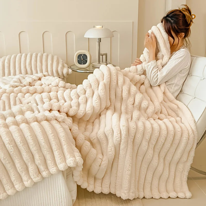 A fluffy cream-colored blanket is draped over a white sofa, with a person adjusting it in a bright room.