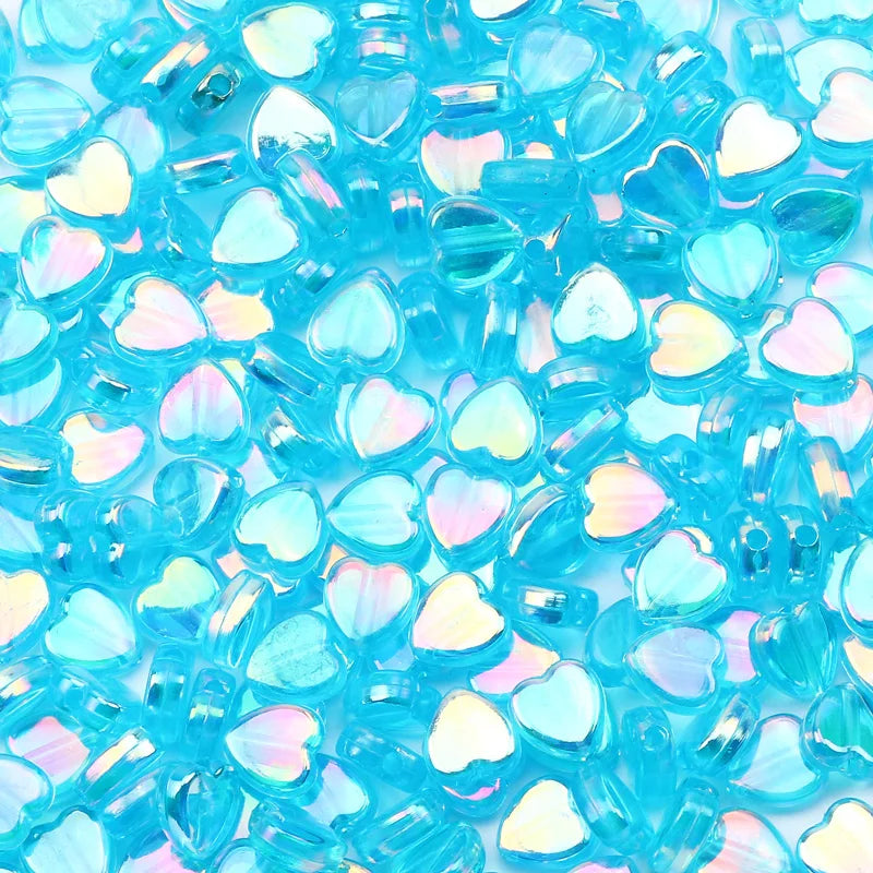 A close-up of a 100-pack of iridescent blue acrylic heart beads for jewelry making.