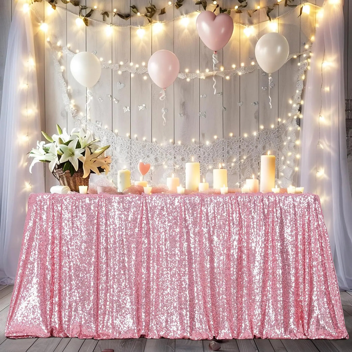 A pink sequin rectangle table cover draped with fairy lights and balloons for a party setting.