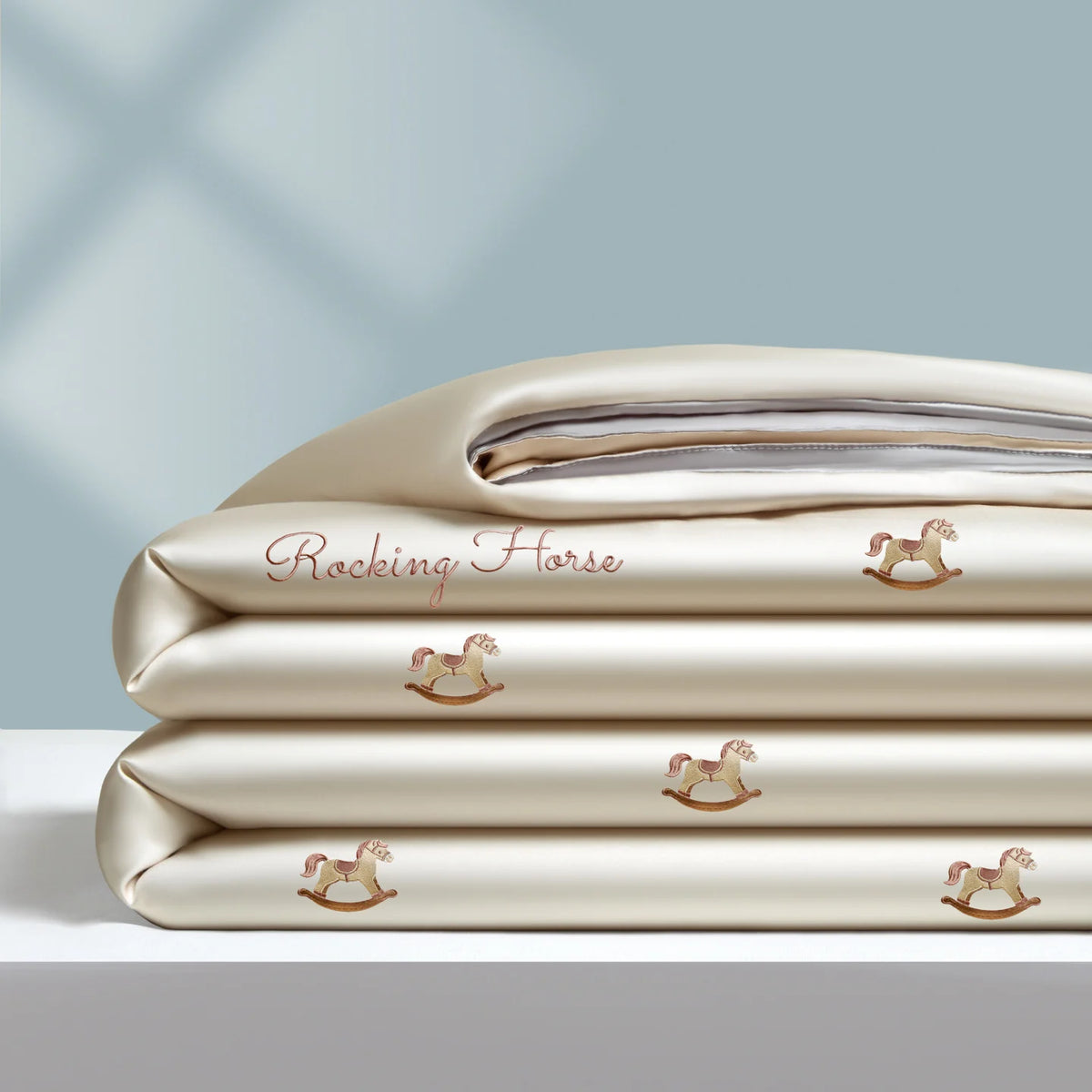 A stack of light beige embroidered cooling summer quilts with small horse designs.