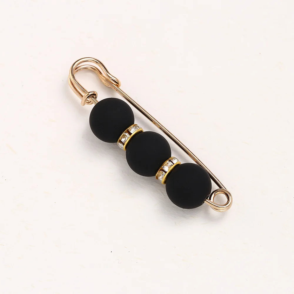Gold-toned adjustable pearl brooch featuring black spherical beads and small clear stones.