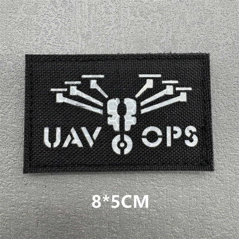 Black embroidered patch with white stylized UAV Ops logo on a gray background