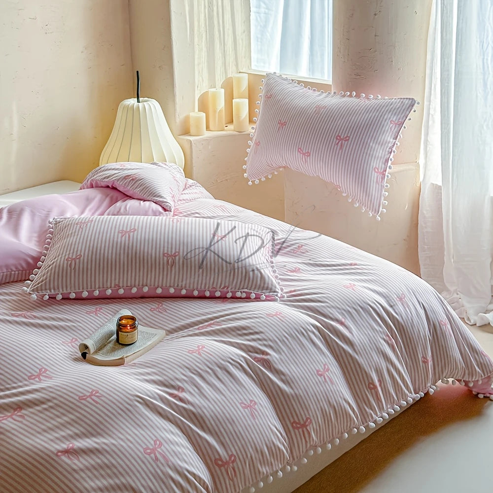 A pink quilt duvet set with striped fabric and decorative bows is displayed on a bed next to a window.