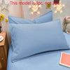 A close-up of a light blue matte solid color pillowcase on a bed, with decorative star lights in the background.
