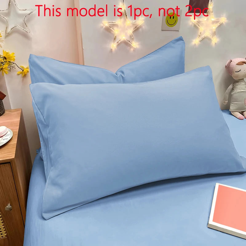 A close-up of a light blue matte solid color pillowcase on a bed, with decorative star lights in the background.
