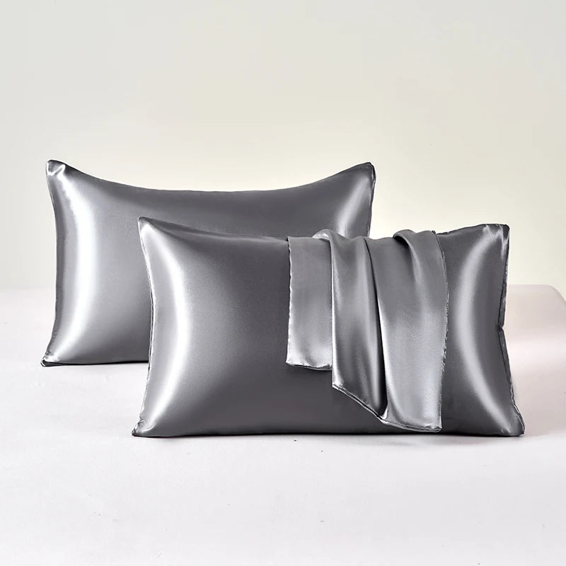 A set of two smooth satin pillowcases in a silver-gray color are displayed on a white surface.