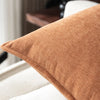 A close-up of a textured, rust-colored chenille throw pillow on a white sofa.