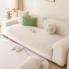 A white sofa covered with a textured, quilted fabric featuring light green accent pillows and decorative floral arrangement.
