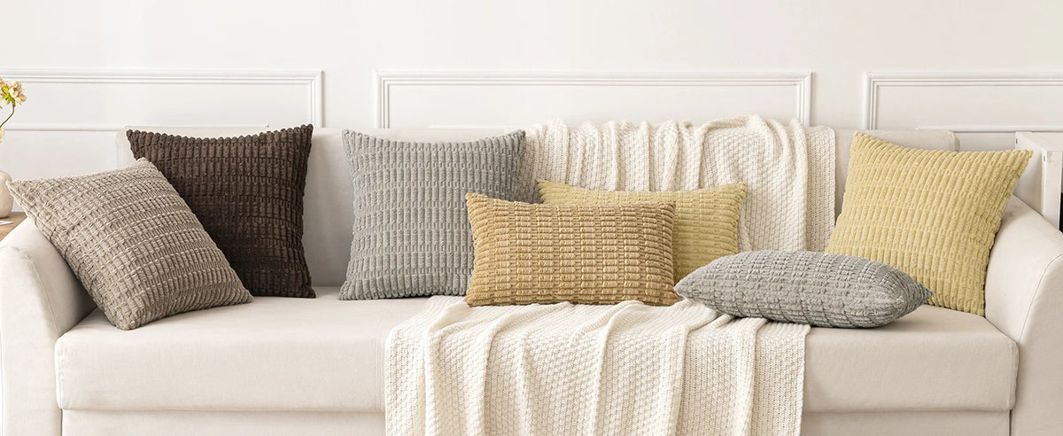 A collection of textured throw pillows in neutral tones including beige, gray, olive green, and brown on a white sofa.