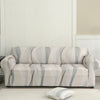 A light beige stretch floral elastic sofa cover displayed on a white floor against a paneled wall.