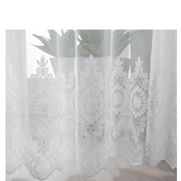 White embroidered floral tulle window curtain hanging in a sheer drape.