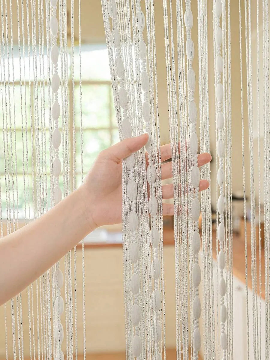 A hand is touching a sheer white beaded string curtain hanging vertically, showing the delicate strands and texture.