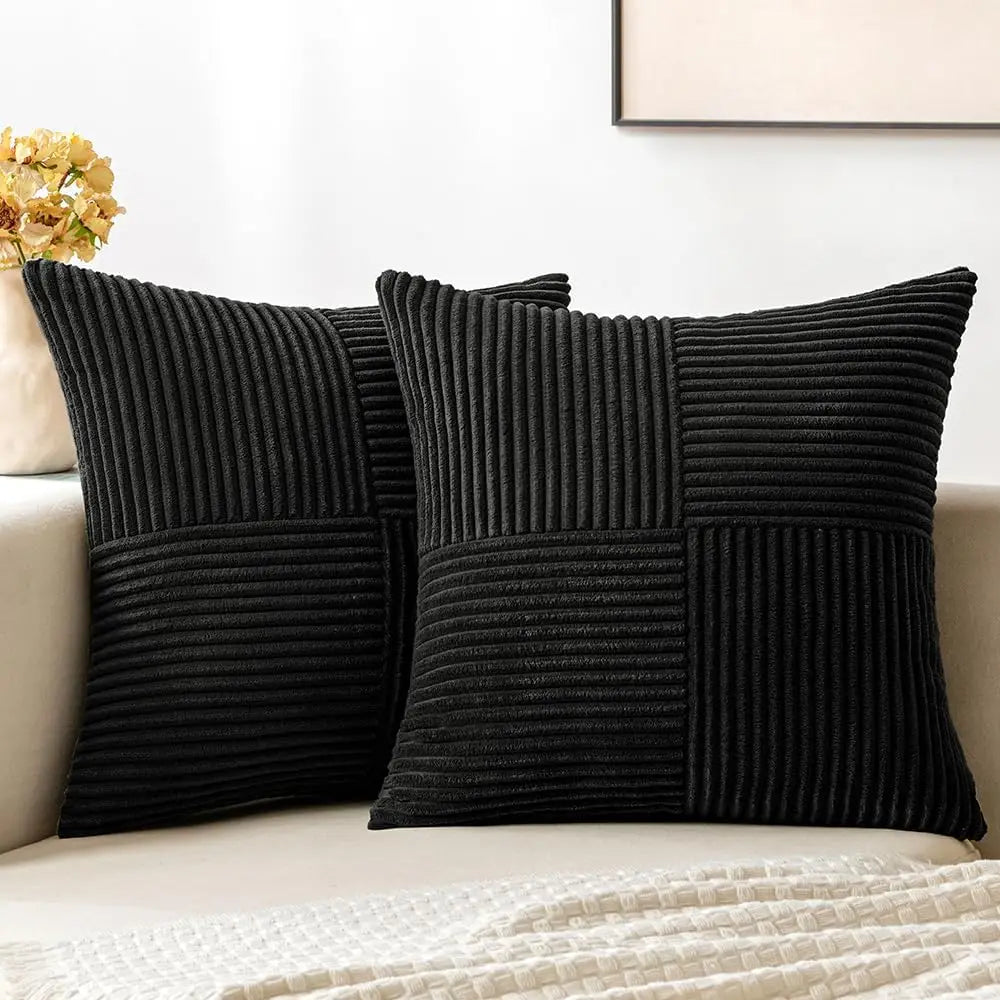 A set of four black neutral corduroy throw pillow covers with a patchwork design displayed on a light sofa.