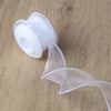 A roll of sheer white organza ribbon unwinding onto a wooden surface.
