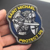 A dark gray embroidered patch featuring a white angel and sword design with the text SAINT MICHAEL PROTECT US in yellow threa