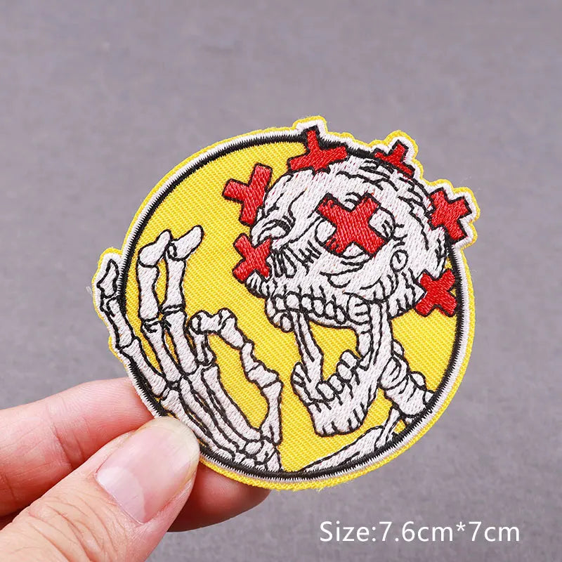 Yellow embroidered patch featuring a white skull with red crosses, showing the detail of skeletal hands.