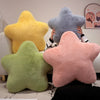 Three star-shaped decorative throw pillows in yellow, gray, and pink are held by a person.